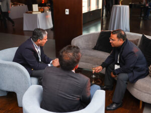 three men sitting on armchairs and a couch discussing business