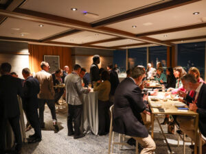 room filled with people standing conversing on one side and people sat eating on the other side