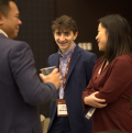 man looking into the camera smiling while speaking with man and woman in suits