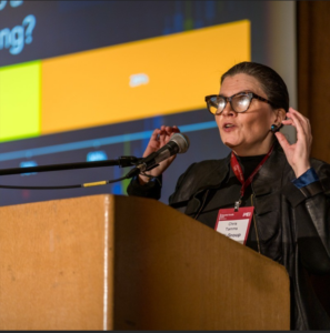 woman with glasses behind a podium speaking